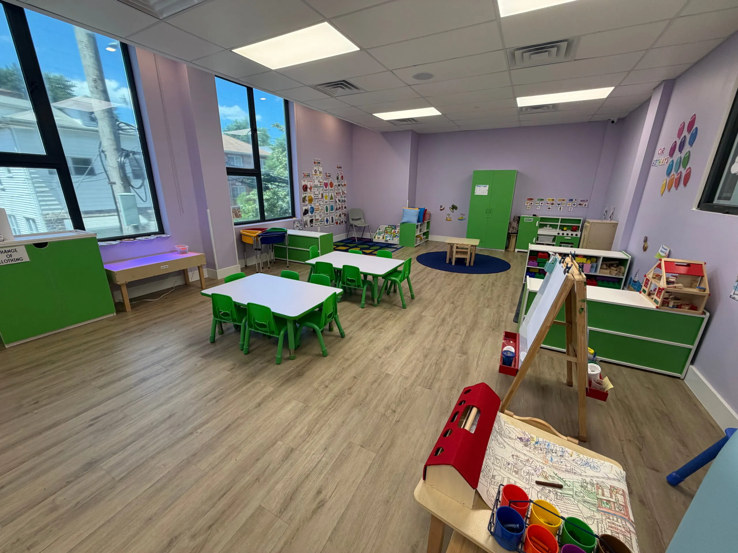 A bright Big Dreams classroom with small tables, shelves and an art easel