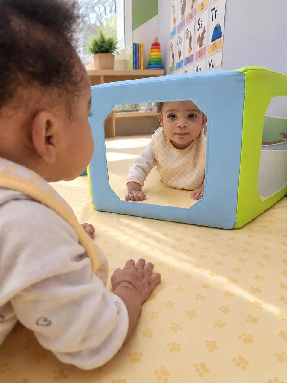 Two babies playing peekaboo through a soft play cube