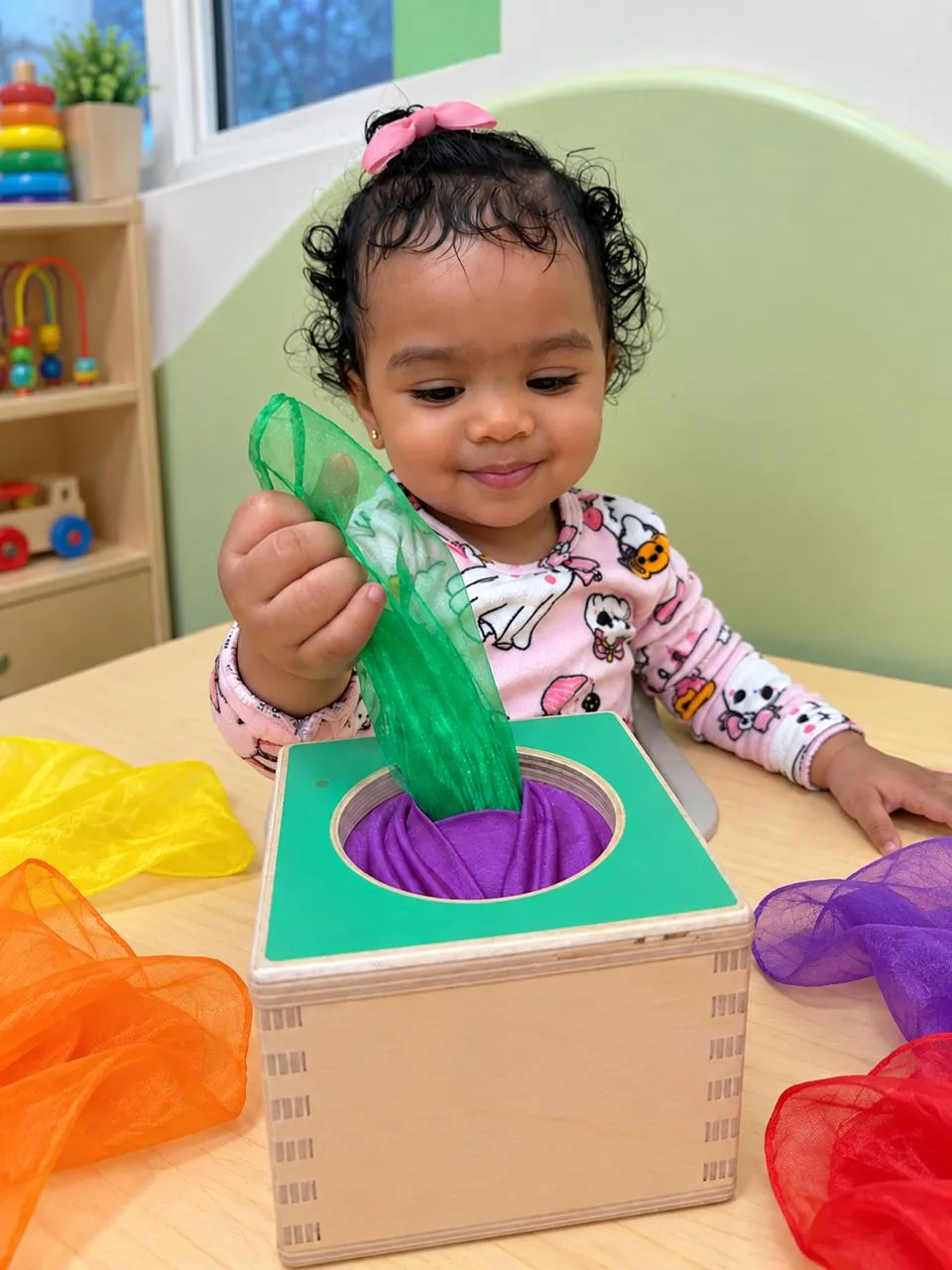 A baby pulling colorful scarves out of a wooden box