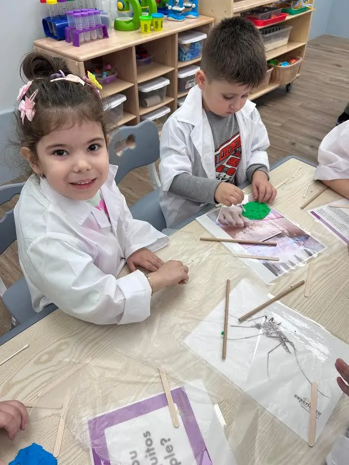 A smiling girl in a lab coat working on a craft-stick project