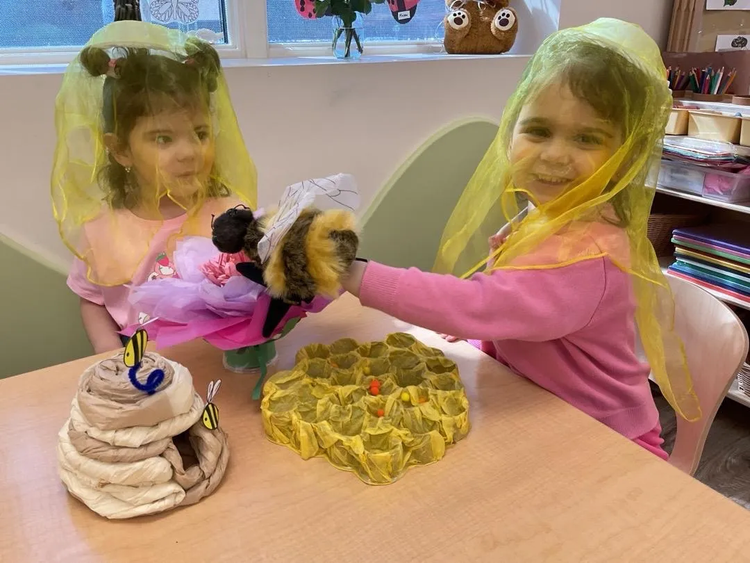 Two preschoolers in yellow veils playing with bee puppets and a honeycomb