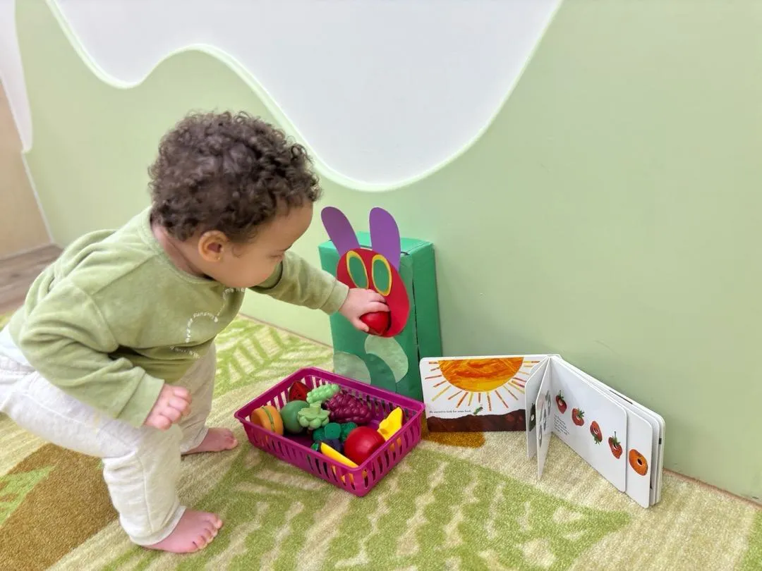A toddler reaching into a basket of play food