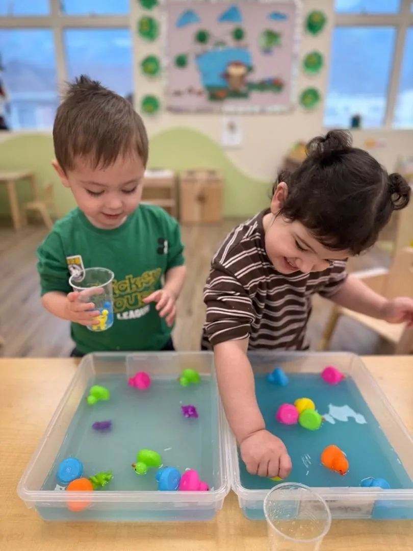 Two toddlers scooping toys at a water table