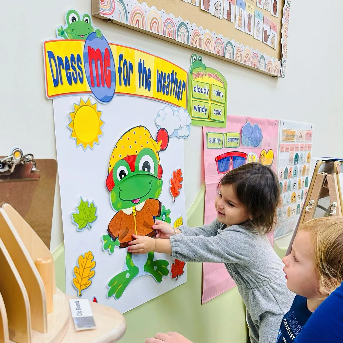 Children dressing a felt frog for the weather on a classroom board