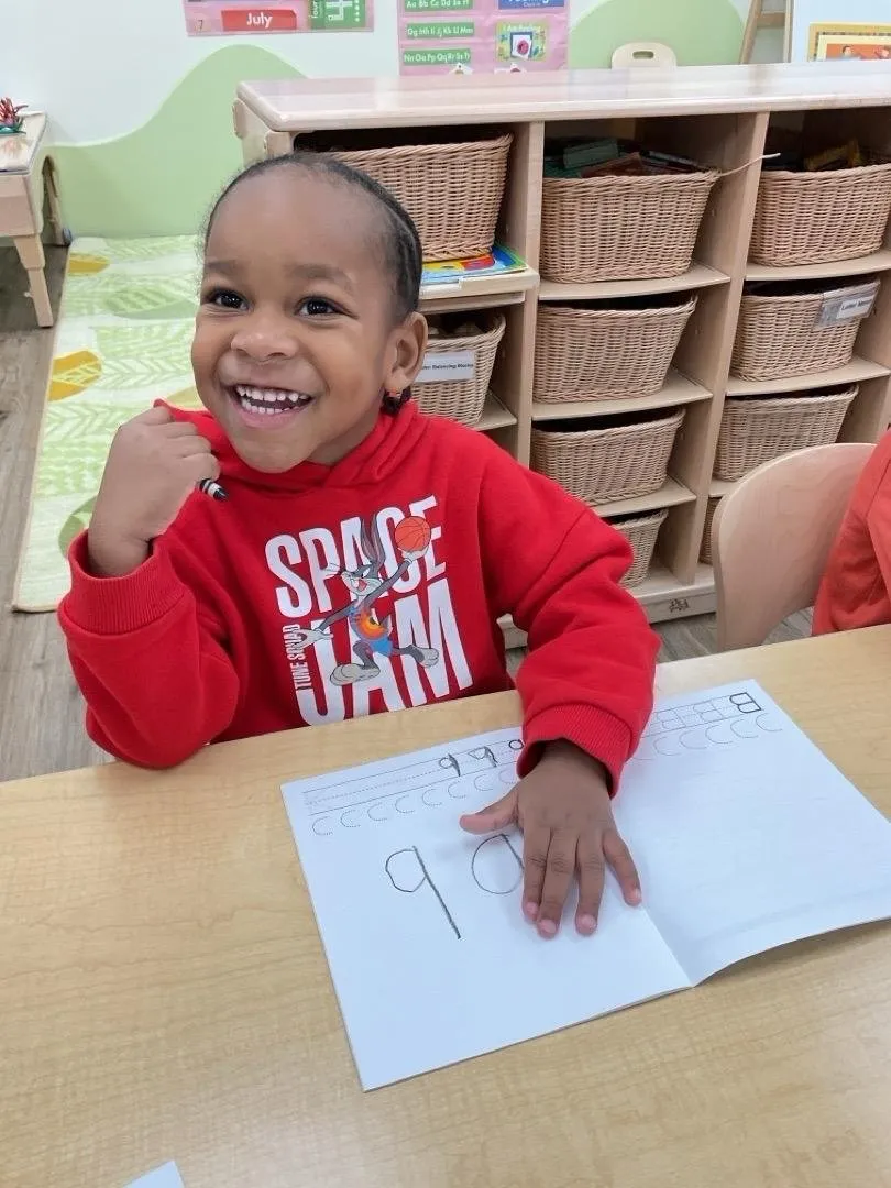A smiling preschooler practicing writing in a workbook